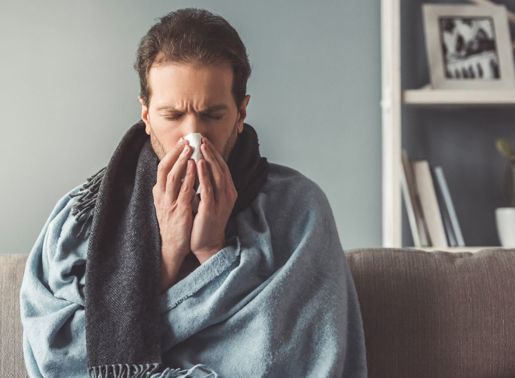 man with pneumonia sneezing into a tissue