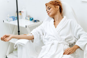 A young woman patient in a white robe relaxing as she enjoys the benefits of an IV drip treatment in a Fort Worth, TX, facility.