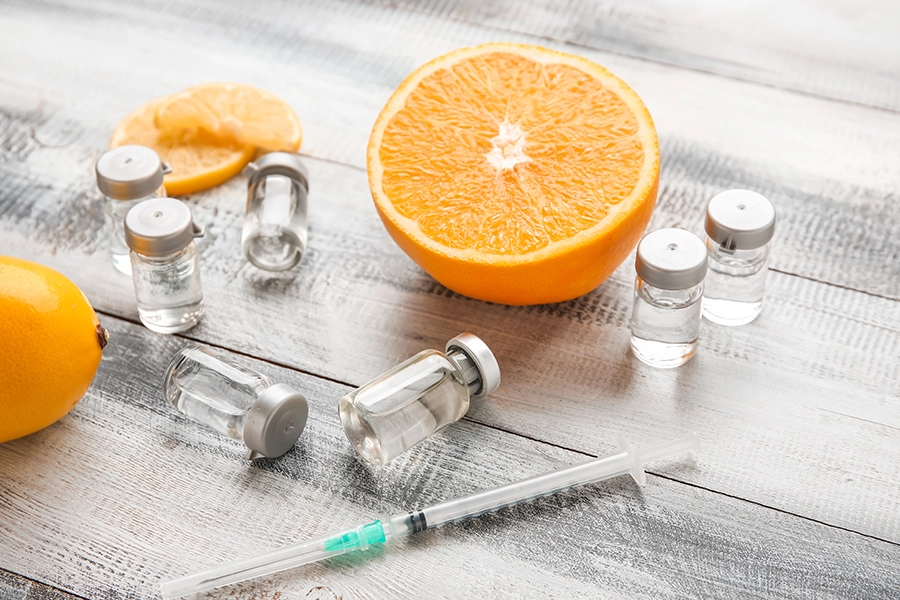 Needle with an orange and syringe bottles sitting on a table representing vitamins in a shot.