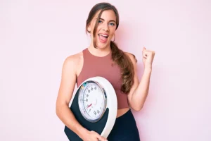 Woman in Farmer's Branch, TX, holding scale happy because she lost weight with Medical Weight Loss Program.